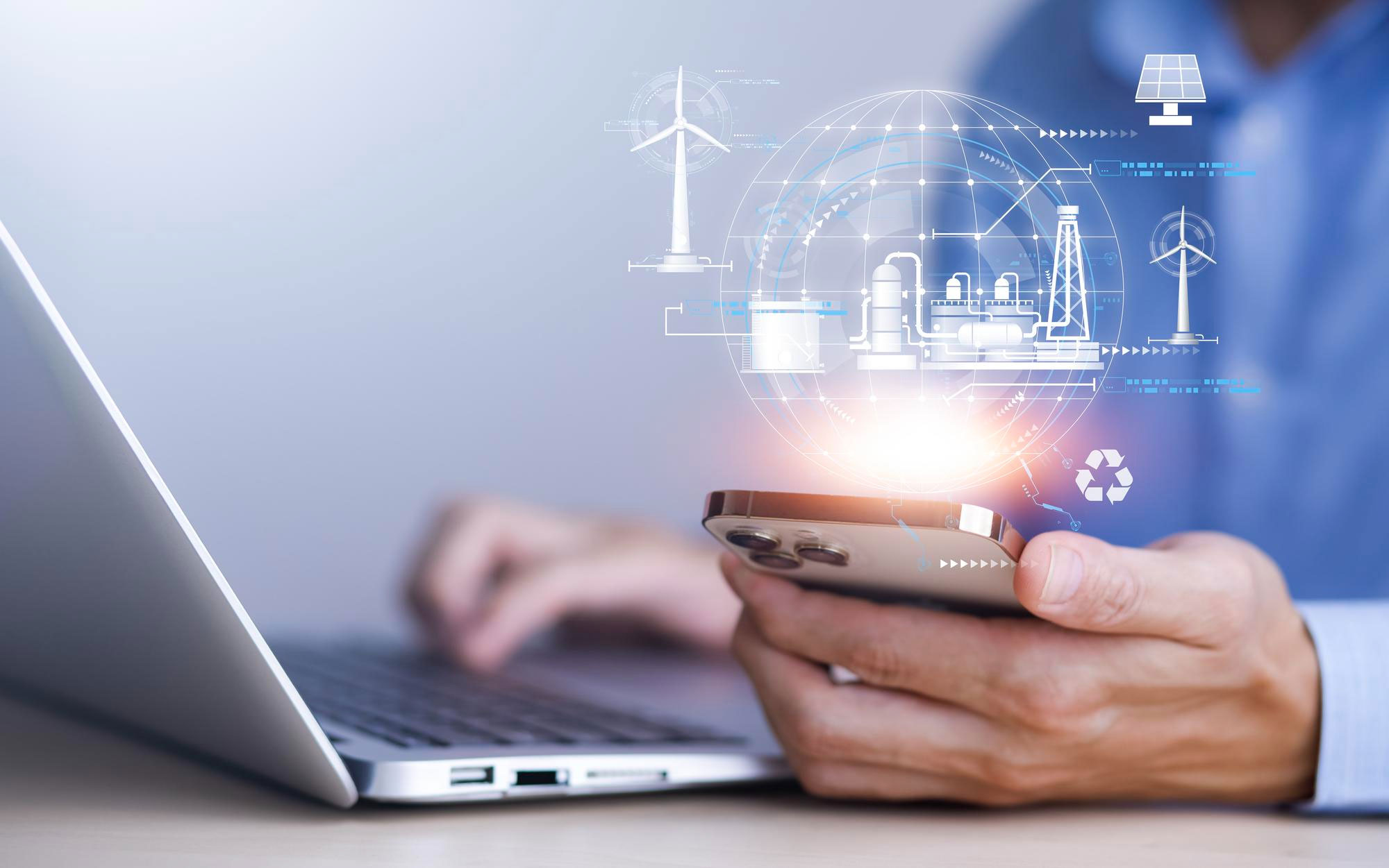 Persona usando un móvil y un portátil con gráficos digitales de energías renovables y sistemas industriales
