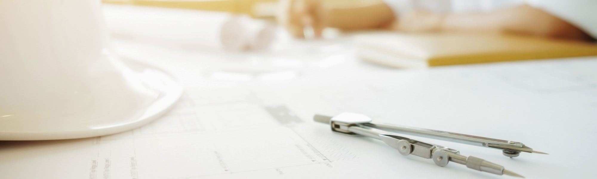 Casco de seguridad y compás de ingeniería sobre planos técnicos en una mesa de trabajo